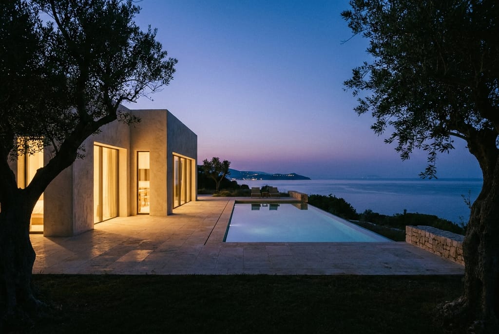 Villa au littoral, heure bleue Villa contemporaine au crépuscule, terrasse face au littoral méditerranéen, mer calme, ciel pourpre, intérieur éclairé en lanterne derrière les baies